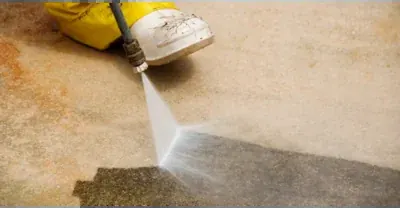 A pressure washer cleaning a stained concrete surface